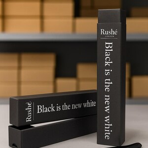 May include: Black toothbrush with black packaging. The packaging has the text "Black is the new white" and the brand name "Rushé London". The toothbrush is black with gray bristles. The background has boxes on a shelf.