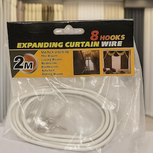 以下が含まれることがあります： 8つのフックが付いた白い拡張カーテンワイヤーキット。「EXPANDING CURTAIN WIRE」と「2M」の文字がパッケージに記載されています。このキットは主に部屋、リビングルーム、寝室、バスルーム、キッチン、ダイニングルームで使用されます。