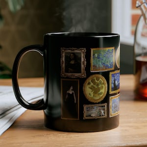 May include: Black ceramic mug featuring framed famous paintings. The mug has a curved handle and is sitting on a wooden surface. Steam rises from the mug, suggesting a hot beverage inside. The mug is surrounded by a newspaper and a glass teapot.