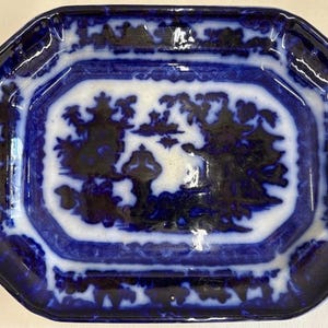 May include: An octagonal blue and white ceramic plate. The plate features a central white panel with a dark blue landscape design. The border is a darker blue with a repeating pattern. A vintage decorative piece.