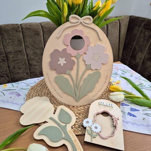 May include: Wooden floral wall art featuring three-dimensional flowers in pink, mauve, and green. The design includes a bow at the top and the text "Happy Mother's Day 2026" and "to mummy love maisie". Additional wooden flower cutouts are also present.