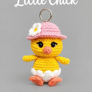 Peut inclure: Un porte-clés Little Chick au crochet représentant un oiseau jaune portant un chapeau rose avec une fleur blanche, un bec et des pattes orange, et une base en coquille d'œuf blanche. Le texte Little Chick et PDF CROCHET PATTERN est visible.