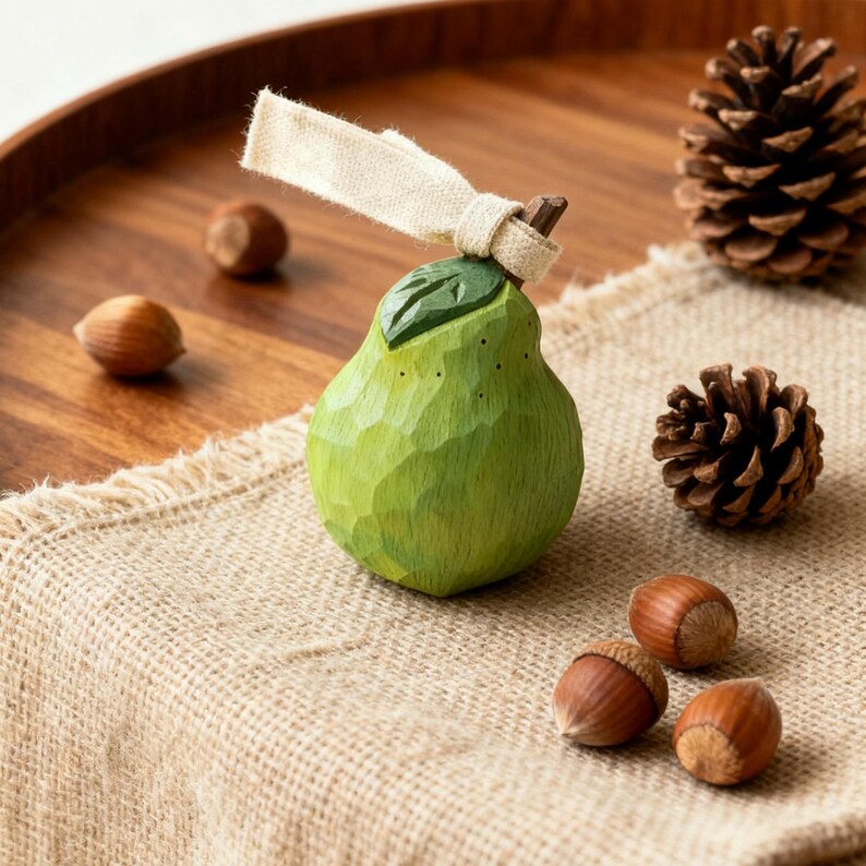 Peut inclure: Ornement en forme de poire en bois vert sculpt&eacute;, avec un ruban beige et des d&eacute;tails de feuilles. Entour&eacute; de noisettes, de pommes de pin et d'un plateau en bois. Id&eacute;al pour la d&eacute;coration int&eacute;rieure.