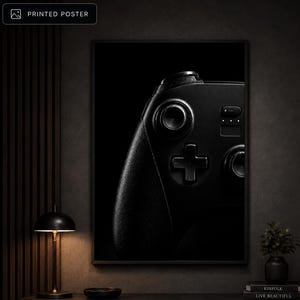 Op de afbeelding: Een rechthoekige gedrukte poster met een contrastrijke, donkergekleurde afbeelding van een videogamecontroller. Het kunstwerk toont de linkerkant van de controller, met de nadruk op de analoge stick, het D-pad en het textuurrijke handvat.
