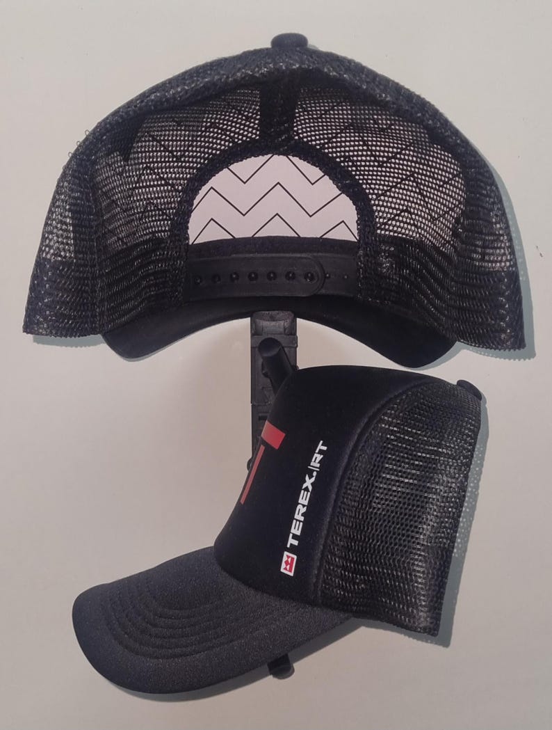 May include: Black trucker hat with a curved brim and mesh back. The hat features the text "TEREX.IRT" in white and red on the front. The back of the hat has a black adjustable snap closure.