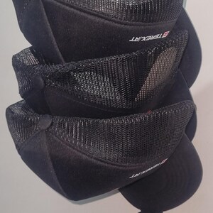 May include: Stacked black baseball caps with mesh netting on the crown. The caps have a curved brim and a button on top. The brand name "TEREX.RT" is printed on the side of the caps. The caps are stacked on top of each other.