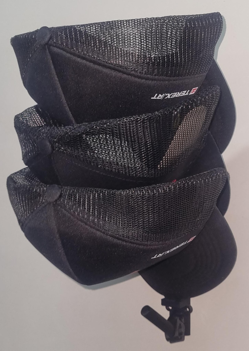 May include: Stacked black baseball caps with mesh netting on the crown. The caps have a curved brim and a button on top. The brand name "TEREX.RT" is printed on the side of the caps. The caps are stacked on top of each other.