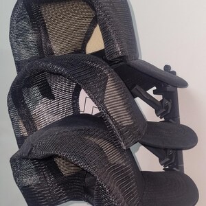 May include: Two black mesh trucker hats are displayed on a black hat rack. The hats have a curved brim and a mesh back. The rack is mounted on a white wall.