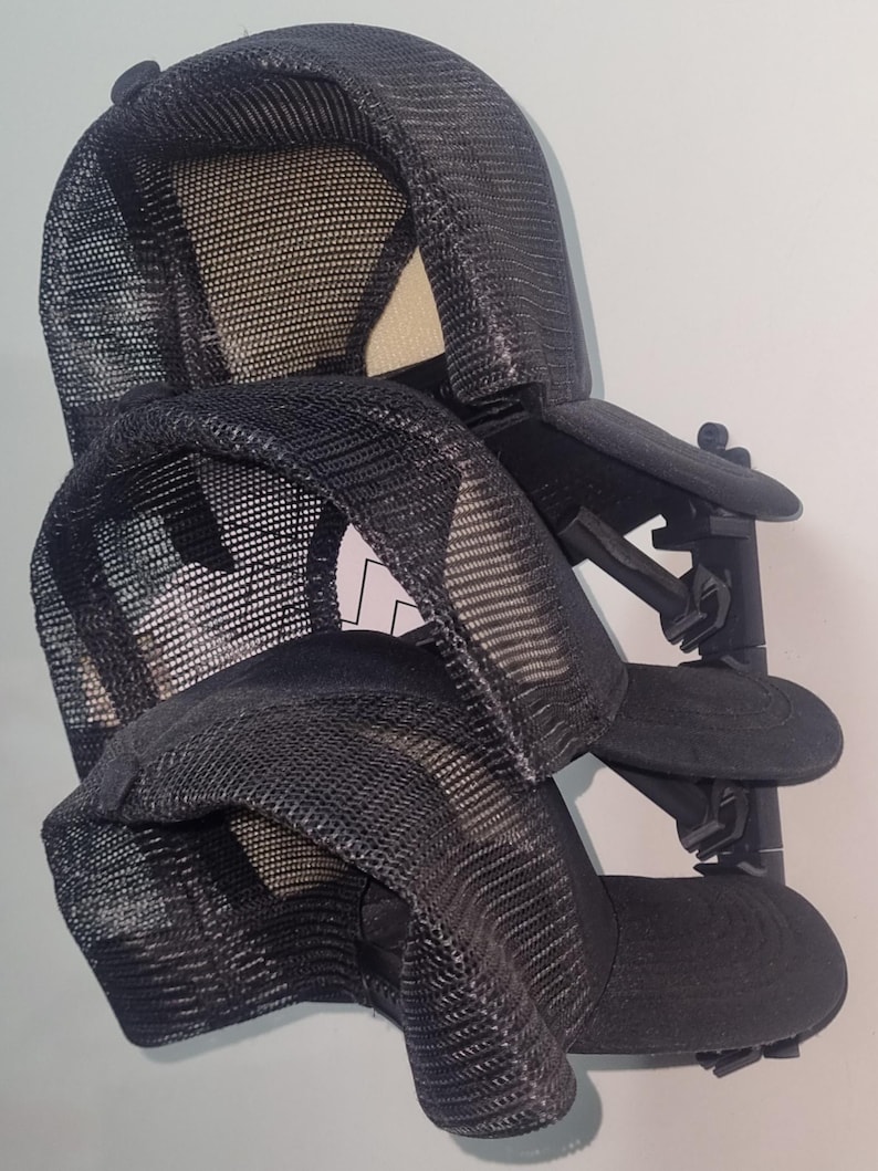 May include: Two black mesh trucker hats are displayed on a black hat rack. The hats have a curved brim and a mesh back. The rack is mounted on a white wall.
