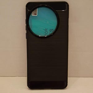 Puede incluir: Funda de teléfono negra con acabado texturizado. La funda tiene una gran abertura circular para la lente de la cámara y una película protectora con el texto "FRONT" y "PROTECTOR". La funda está diseñada para proteger el teléfono.