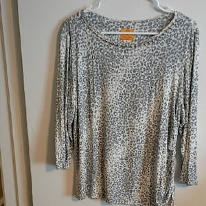 May include: A long-sleeved, scoop-neck top with a gray and white leopard print pattern. The neckline is embellished with small, silver-colored beads. The top is hanging on a white hanger.