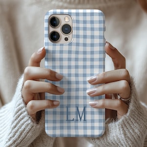 May include: A light blue and white gingham patterned phone case with the initials "LM" in a matching blue font. The case is held in front of a neutral background.