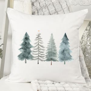 May include: White square throw pillow featuring a watercolor design of four Christmas trees in shades of blue and gray. One tree has a gold star on top. The trees are arranged in a row on the pillow.