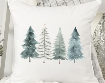 May include: White square throw pillow featuring a watercolor design of four Christmas trees in shades of blue and gray. One tree has a gold star on top. The trees are arranged in a row on the pillow.