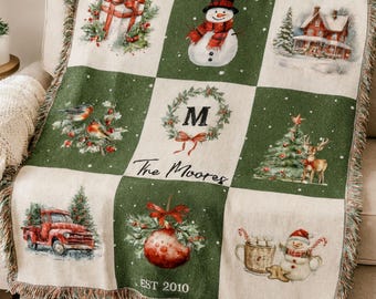 May include: A personalized Christmas blanket with a patchwork design featuring Christmas-themed illustrations. The blanket has a green and cream color scheme, with images of a snowman, a red truck, and a Christmas tree. The text "The Moores" and "EST 2010" are also visible.