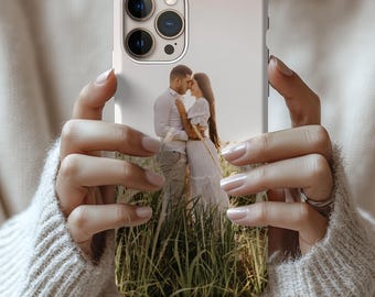 May include: A white phone case featuring a photograph of a couple embracing in a field of tall grass. The phone case has a camera cutout and the text "Personalized photo phone case!" at the bottom.