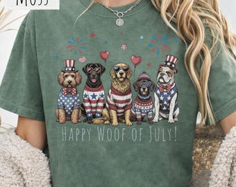 May include: A moss green t-shirt featuring a graphic of five dogs wearing patriotic sweaters, hats, and heart-shaped sunglasses. The design includes red and blue fireworks, balloons, and the text "HAPPY WOOF OF JULY!" printed in white.