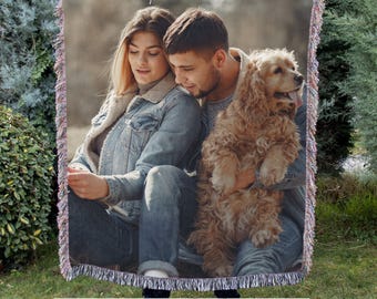 May include: Woven blanket featuring a photograph of a couple and a dog. The blanket has a fringed edge and displays the text "Give them the gift of memories captured on a STUNNING blanket!"
