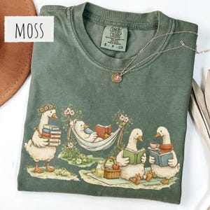 Cute cottagecore reading goose shirt showing four geese enjoying books hammock reading tea and cozy outdoor reading scenes perfect book lover gift and book club shirt for readers