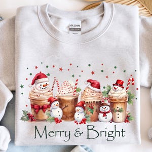 Festive Christmas Sweatshirt Coffee Cup Design Holiday Apparel Collection Merry Bright Saying Snowman Whipped Topping Holly Berry Decoration Candy Cane Accent Winter Seasonal Wear Comfortable Cotton Blend Multiple Size Options Holiday Party
