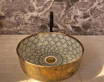 May include: A decorative, round bathroom sink with a gold-colored exterior and a green and white patterned interior. The sink has a dark faucet and is set against a textured background.