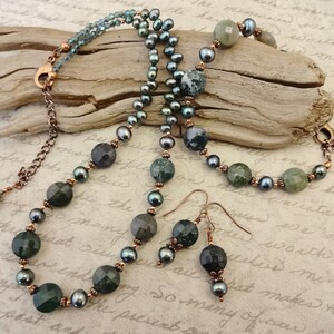 May include: A set of green and black agate gemstone jewelry, including a necklace, bracelet, and earrings. The necklace and bracelet feature copper chain accents. The earrings are dangle style with copper accents.