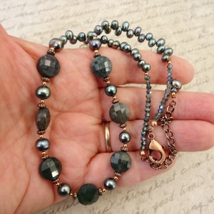 May include: A dark green gemstone necklace with copper accents and black pearls. The necklace has a lobster clasp closure.
