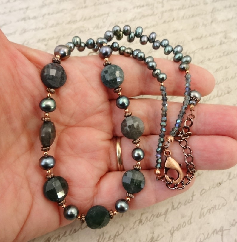 May include: A dark green gemstone necklace with copper accents and black pearls. The necklace has a lobster clasp closure.