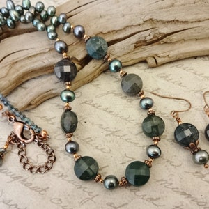 May include: A necklace and earrings set featuring dark green faceted gemstone beads, black pearls, and copper accents. The necklace has a lobster clasp closure.