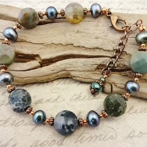 May include: A bracelet made with green and gray agate stones, black pearls, and copper beads. The bracelet has a lobster clasp closure.