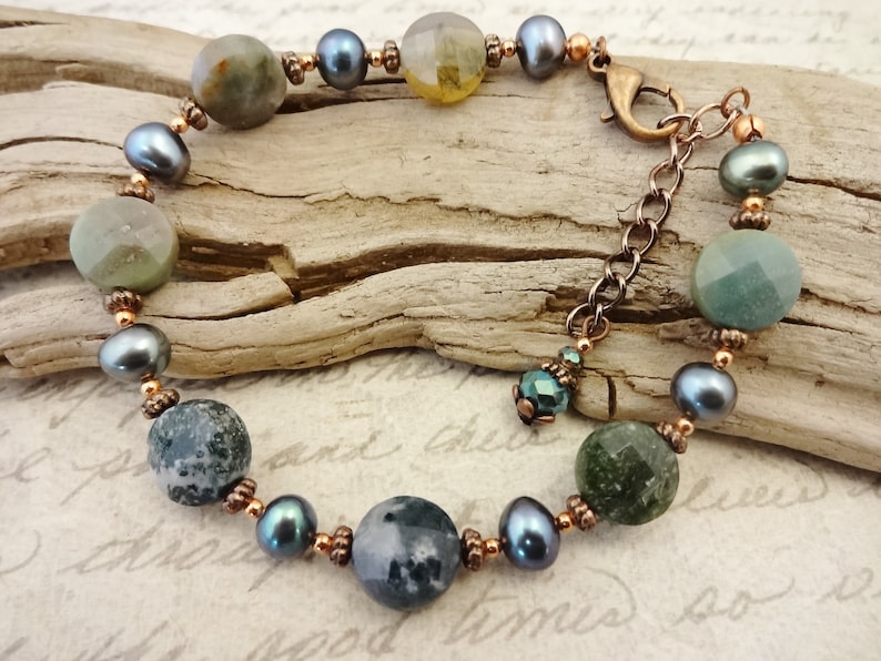 May include: A bracelet made with green and gray agate stones, black pearls, and copper beads. The bracelet has a lobster clasp closure.