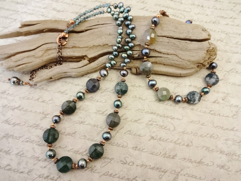 May include: A multi-strand necklace with green agate beads, freshwater pearls, and copper spacers. The necklace is displayed on a piece of driftwood.