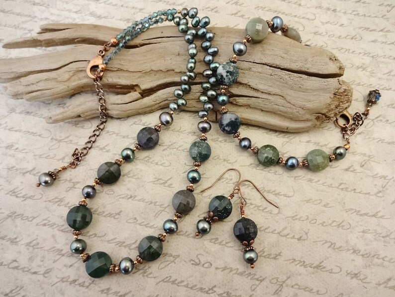 May include: A set of green and black agate gemstone jewelry, including a necklace, bracelet, and earrings. The necklace and bracelet feature copper chain accents. The earrings are dangle style with copper accents.