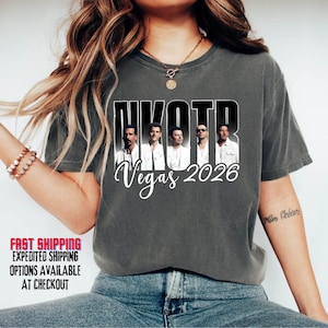 May include: Dark gray t-shirt featuring a graphic of a musical group with the text "NKOTB Vegas 2026". The shirt has a crew neck and short sleeves. The image is centered on the front of the shirt.