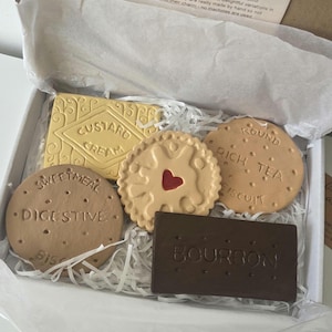 May include: A set of five biscuit-shaped coasters in a white box with white paper filler. The coasters include a rectangular yellow Custard Cream, a round tan Sweetmeal Digestive, a round tan Round Rich Tea, a round tan Jam Ring, and a rectangular dark brown Bourbon.