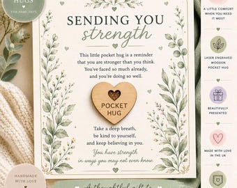 May include: A light-colored card featuring green botanical illustrations and the text "SENDING YOU strength". A small, light-brown wooden heart with a cutout and the words "POCKET HUG" is attached to the center. The card includes encouraging text.