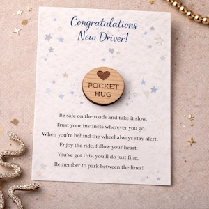 May include: A greeting card with the text "Congratulations New Driver!" and a wooden pocket hug. The pocket hug is round with a heart and the words "POCKET HUG". The card has a light blue star pattern.