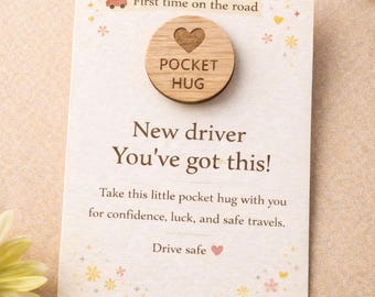 May include: A wooden pocket hug with a heart design, attached to a card. The card reads "First time on the road" and "New driver, You've got this!" with a message about confidence and safe travels. The card has floral and car graphics.