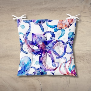 May include: A square seat cushion featuring a white background with a watercolor print of blue and purple octopuses and sea turtles. The cushion includes four white fabric ties at the corners for securing it to a chair or bench.