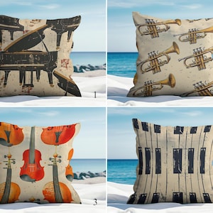 Puede incluir: Cuatro cojines decorativos con diseños de instrumentos musicales. Uno presenta un piano, otro trompetas, un tercero violines y el último un teclado de piano. Los cojines están en una playa de arena con el océano de fondo.