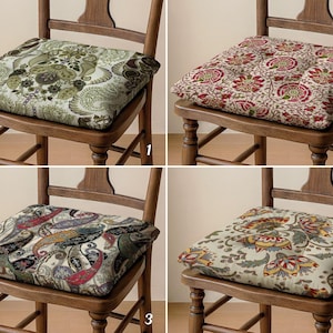 Puede incluir: Cuatro cojines cuadrados para silla sobre sillas de madera, cada uno con un patrón distinto. El cojín 1 tiene un estampado de cachemira verde, el 2 un diseño floral rojo y crema, el 3 muestra un motivo de cachemira multicolor y el 4 un patrón floral.