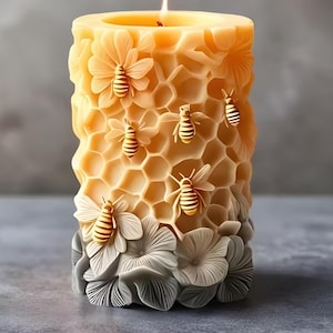 May include: A cylindrical candle with a honeycomb and bee design. The candle is primarily yellow with detailed relief carvings of bees and honeycomb cells. The base features grey floral accents, and the candle is lit with a visible flame.