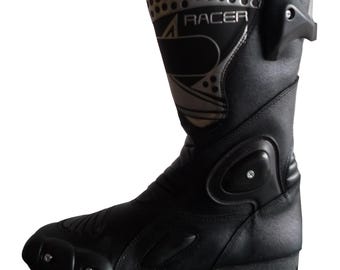Könnte beinhalten: Schwarzer Motorradstiefel mit dem Wort "RACER" in silbernen Buchstaben. Der Stiefel hat eine verstärkte Zehen- und Knöchelpartie, silberne Akzente und eine Schutzplatte an der Seite. Der Stiefel ist aus Leder gefertigt und hat einen hohen Schaft.