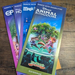 Puede incluir: Una pila de coloridos mapas de los parques de Disney. El mapa de Animal Kingdom presenta una vibrante ilustración de los personajes de Zootopia. Otros mapas incluyen EPCOT, Hollywood Studios y Magic Kingdom. El mapa de Zootopia también incluye el texto "GUIDEMAP".