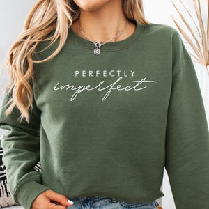 May include: A white ceramic mug with a black handle and the text "But First, Coffee" in a bold, black font. The mug is set against a blurred background, suggesting a cozy setting.