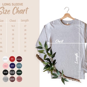 May include: A light gray long-sleeve shirt hanging on a wooden hanger, with a size chart and color swatches to the left. The size chart shows chest and length measurements in inches. A sprig of greenery is draped across the shirt.