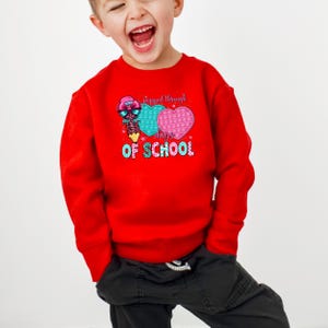 May include: A red sweatshirt with a graphic that says "Flipped through days OF SCHOOL". The graphic includes a pencil, two heart-shaped pop-it toys, and stars. The sweatshirt is worn by a child.