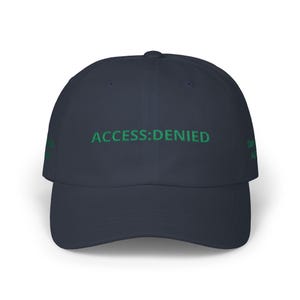 May include: A navy blue baseball cap featuring the green embroidered text "ACCESS:DENIED" across the front. The cap has a curved peak and a six-panel design. The phrase "OWN ME" is also embroidered on the side.