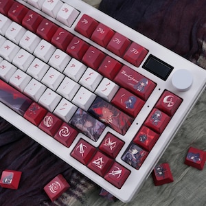 May include: A white mechanical keyboard with red and white keycaps. The keycaps feature various designs and illustrations, including anime-style characters and symbols. The keyboard has a volume knob and a small display screen.