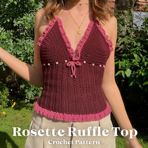 Puede incluir: Top halter de ganchillo burdeos con ribete rosa con volantes y detalle de lazo. El top está adornado con pequeñas cuentas blancas y presenta el texto "Rosette Ruffle Top Crochet Pattern" en blanco.